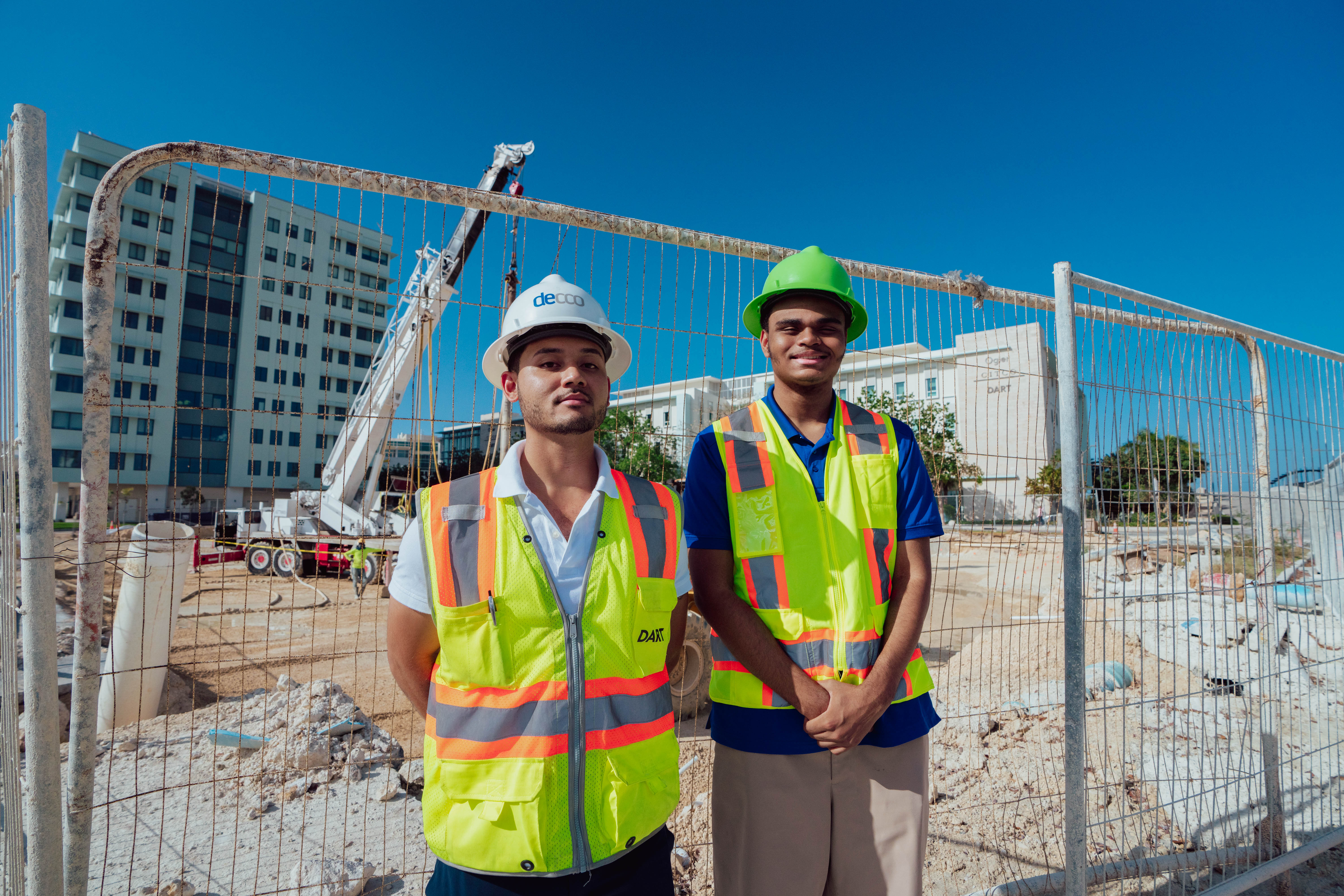 Two men standing in front of construction site with PPE on. 